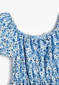 Blau-weißes Blumenkleid mit kurzen Puffärmelchen, elastischem Ausschnitt und kleiner Schleife in der Mitte vorne.