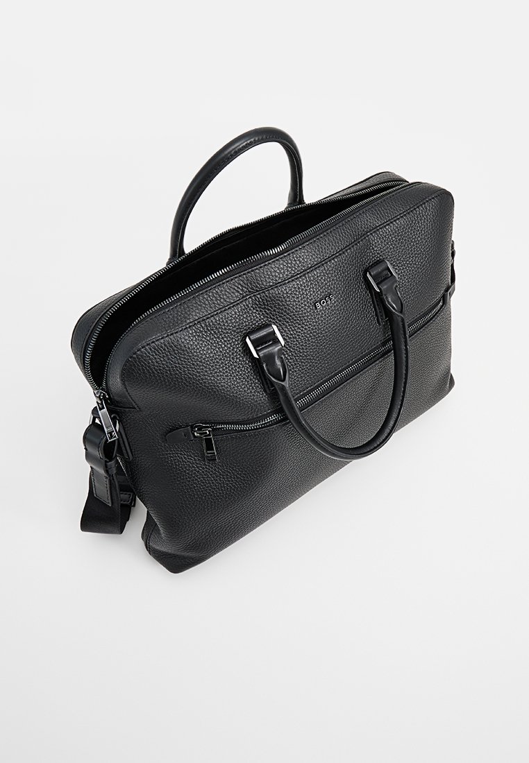 Serviette en cuir noir avec une surface texturée. Dispose de doubles poignées et d'une bandoulière amovible. Comprend une poche zippée à l'avant.