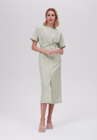 Stripet midi-kjole i lys grønn og hvit, med vridd liv, korte ermer og splitt foran. Brukt med hvite sandaler.