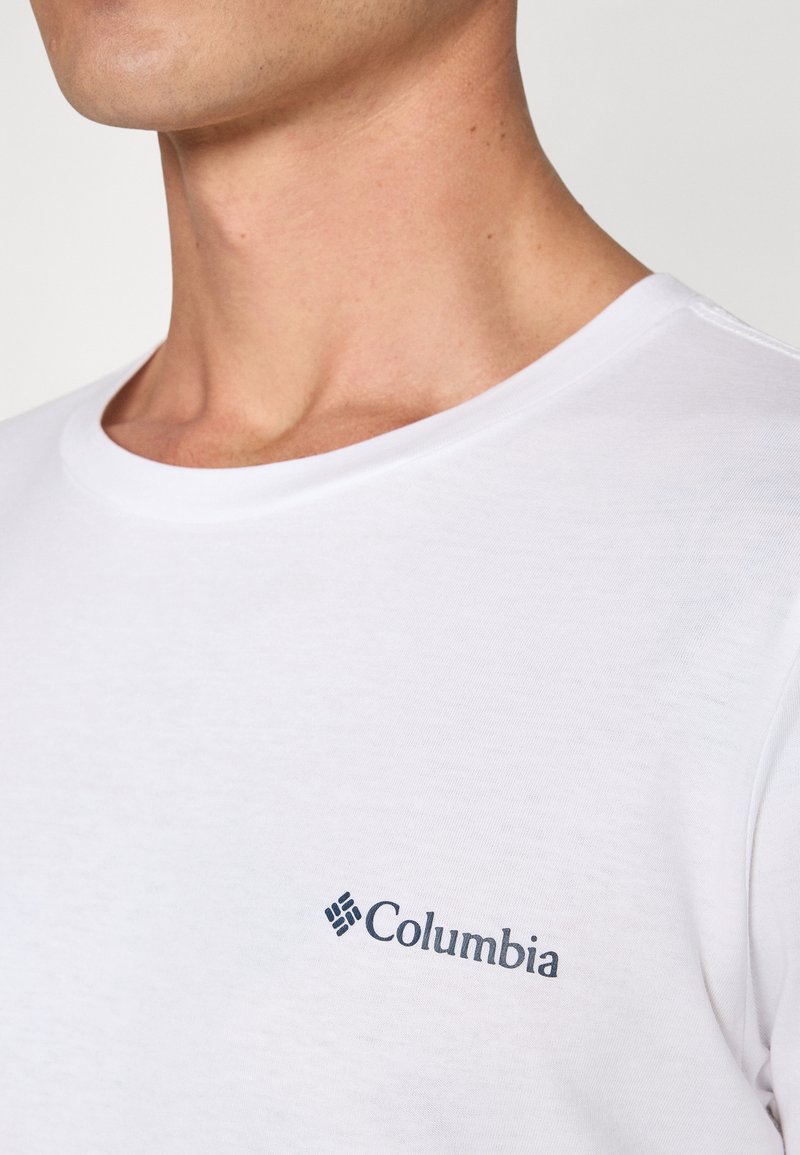 Weißes Kurzarm-T-Shirt aus Baumwolle, mit Rundhalsausschnitt und kleinem blauen Columbia-Logo auf der linken Brust. Glatte Textur.