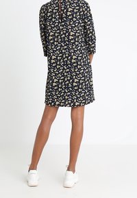 Sukienka w kwiatowy wzór w granatowym kolorze z rękawami trzyczwartowymi, z rozcięciem z tyłu i białymi trampkami. Posiada drobne żółte i białe kwiaty.