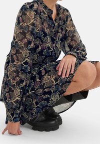 Dunkelmarineblaues Blumenkleid mit transparenter Textur, das von mehrfarbigen Blumenmustern und Knopfdetails geprägt ist, kombiniert mit schwarzen klobigen Stiefeln.