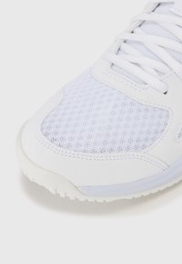 Hvid sportssko med en mesh-overdel, glatte syntetiske overflader og en tekstureret gummisål. Snørebåndene er vævet gennem øjerne.