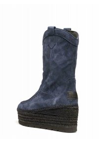 Modré semišové wedges boty s vysokou pletenou platformou a poutky na vrchu, nakloněné, aby ukázaly vnější stranu a zadní část.