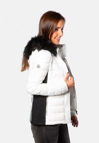 Veste d'hiver rembourrée avec un corps blanc et des côtés côtelés noirs, dotée d'une capuche en fausse fourrure noire. Fermeture éclair et logo sur la manche gauche.