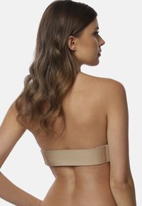 Nude bandeau beha met een gladde, gestructureerde afwerking en een eenvoudig ontwerp, voorzien van een brede band op de rug en minimale hardware.