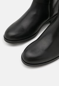 Stivaletti neri in pelle con una texture liscia, punta rotonda e dettagli con cerniera laterale. Presentano un tacco basso e robusto e un design semplice.