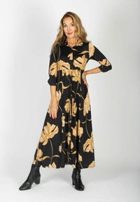 Czarna sukienka w kwiaty z beżowym wzorem, zapinana na guziki, z rękawami o długości trzech ćwierci, zwiewna spódnica, noszona z czarnymi botkami za kostkę.