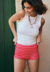 Hvid ribbet tanktop kombineret med pink og hvide stribede shorts, med en tæt pasform og tekstureret stof. Tilbehør inkluderer en perlekæde.