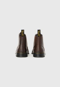 Bottines en cuir marron avec semelles en caoutchouc noires, coutures jaunes et anses de tirage marquées "AVEC DES SEMELLES ÉLASTIQUES."