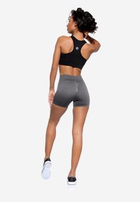 Top corto a coste nero con design racerback, abbinato a pantaloni corti grigi a vita alta. Modella che indossa sneaker nere, di spalle rispetto alla macchina fotografica.