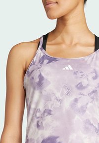 Lilla atletisk tanktop med blomsterprint, let stof, racerback-design, med tre hvide striber logo på brystet.