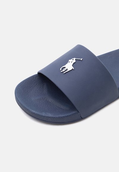 Σανδάλι σλάιντ σε ναυτικό μπλε με υφή στη σόλα και φαρδιά λωρίδα που φέρει λευκό λογότυπο παίκτη πόλο πάνω σε άλογο.
