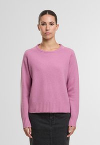 Rosa gestrickter Pullover mit rundem Halsausschnitt, gerippten Bündchen und Saum. Weiche Textur, lockere Passform und abgefallene Schulternähte. Einfaches Design.