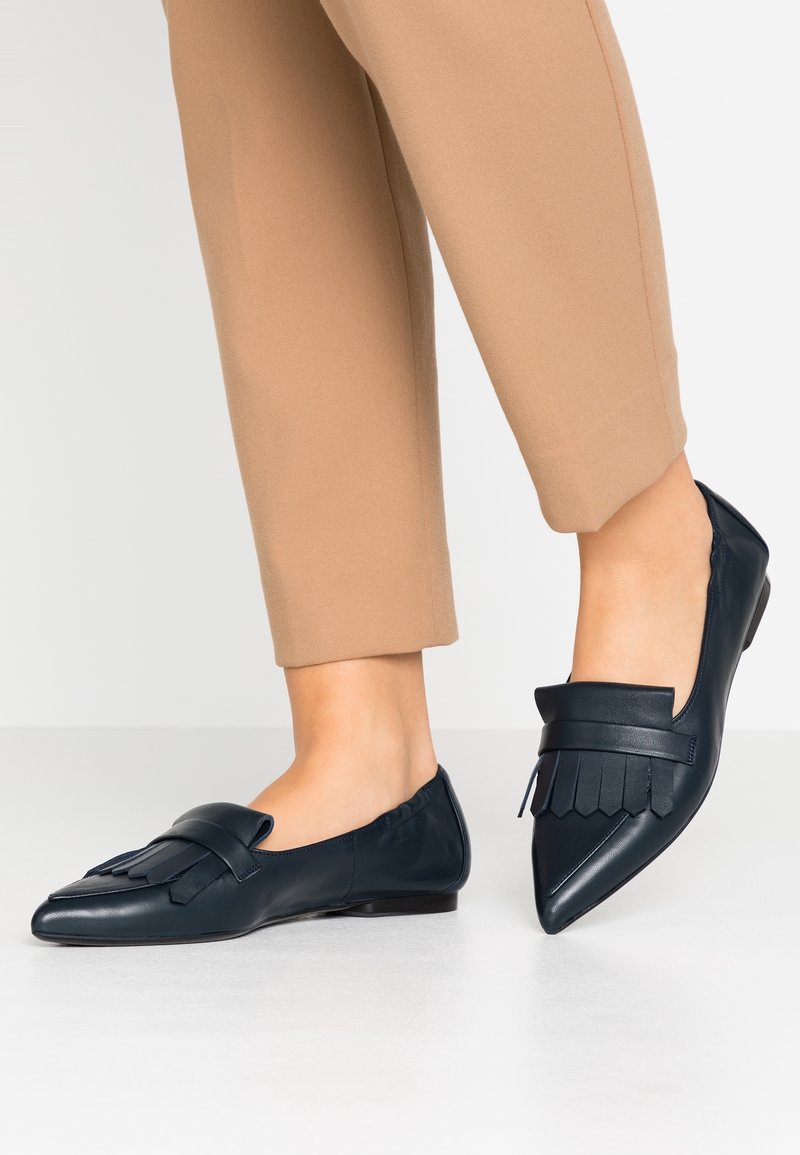Mocassins en cuir bleu marine avec un bout pointu, dotés d'une frange décorative et d'un talon plat. Surface texturée et finition lisse sur l'ensemble.