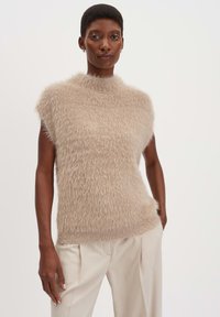 Top in maglia beige con collo alto, maniche corte e una texture morbida e pelosa. Abbinato a pantaloni chiari a pieghe.