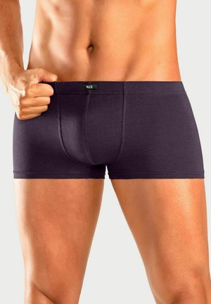 Männlicher Oberkörper und Oberschenkel in dunkelblauen Boxershorts, mit linker Hand, die den Bund an einem hellen Hintergrund hält.