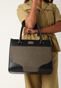 Svart strukturerad handväska med vävt beigt mönster, släta läderdetaljer och guldhårdvarulogga. Dubbla handtag för bärande.