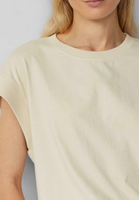 Katoenen T-shirt in lichtbeige, met een ronde hals en opgerolde mouwen, voorzien van een zachte textuur en een losse pasvorm.