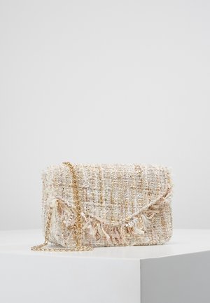 Kremfarvet vævet tweed clutch med frynser og guldfarvet kæderem, hvilende på hvid piedestal mod grå baggrund.