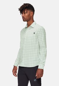 Camicia a maniche lunghe a quadri verde chiaro con quadrati bianchi e verde scuro, bottoni frontali e taschino sul petto con dettagli del logo.