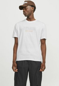 Hvid bomulds-T-shirt med teksten "Jack & Jones Ninety Nineteen" i grå med orange accent. Sammen med sorte cargo bukser.