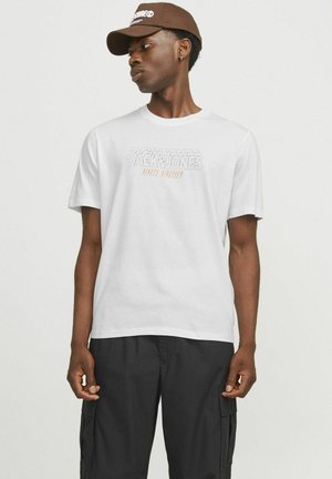 Hvid bomulds-T-shirt med teksten "Jack & Jones Ninety Nineteen" i grå med orange accent. Sammen med sorte cargo bukser.
