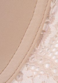 Beige Stoff mit einer strukturierten, gerippten Oberfläche oben, übereinander geschichtet mit zarter Spitze mit floralen Mustern in einem hellrosa Farbton.