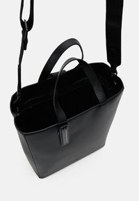 Czarna skórzana torba typu tote z dwoma krótkimi uchwytami i odczepianym długim paskiem. Posiada zamek błyskawiczny, gładką teksturę oraz przywieszkę.