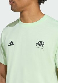 Light green short-sleeve t-shirt made of soft fabric. Features black Adidas logo on the chest and three black stripes on the left shoulder.