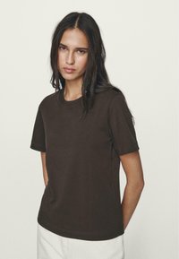 Brun bomulds t-shirt med korte ærmer, rund hals og en afslappet pasform. Glat tekstur uden synlige mønstre eller accenter.