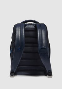 Mochila azul marino con textura acolchada, correas de cuero liso y herrajes metálicos. Cuenta con cierre de cremallera y detalles en azul.