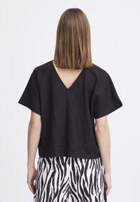 Top nero a maniche corte con scollatura a V sulla schiena, vestibilità ampia, realizzato in un tessuto testurizzato, abbinato a pantaloni con stampa zebra bianco e nero.