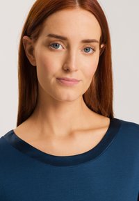 Top azul marino con una textura suave, que presenta un escote ancho y redondeado y acentos satinado en el cuello.