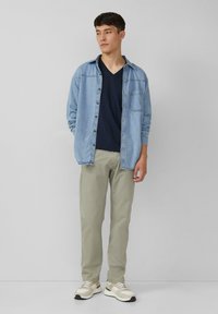 Jasnoniebieska koszula dżinsowa, granatowy t-shirt z dekoltem w serek, khaki spodnie oraz beżowe sneakersy. Koszula ma kieszeń z przodu i zapięcie na guziki.