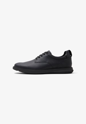 Zapatilla casual negra con cordones, parte superior texturizada, cuello acolchado y suela de goma, mostrada de perfil sobre fondo blanco.