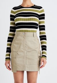 Geribbelde lange mouw top in zwart, olijfgroen en crème strepen; gecombineerd met een beige utility rok met voorzakken en een zijstrikdetail.