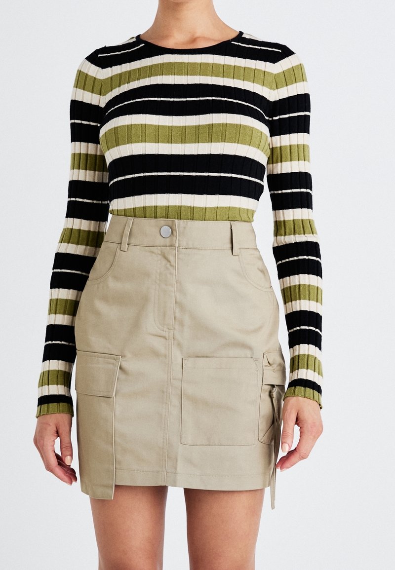 Geribbelde lange mouw top in zwart, olijfgroen en crème strepen; gecombineerd met een beige utility rok met voorzakken en een zijstrikdetail.