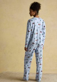 Súprava pyžama z svetlomodrej látky s opakujúcim sa vzorom červených kamiónov a zelených stromov. Dlhé rukávy a nohavice s voľným strihom.