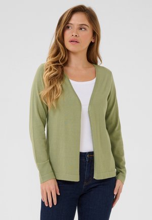 Hellgrüner Cardigan aus weichem Strickmaterial, mit V-Ausschnitt, offener Vorderseite und langen Ärmeln, kombiniert mit einem weißen Hemd und dunklen Jeans.
