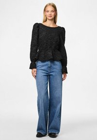 Czarna teksturowana bluzka peplum z długimi puff sleeves i okrągłym dekoltem, w połączeniu z luźnymi niebieskimi dżinsami i czarnymi butami.