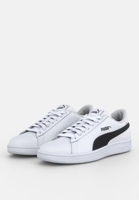 Paire de baskets blanches Puma avec bande latérale noire, lacets blancs et logo Puma sur la languette et le côté, présentée sur un fond blanc.