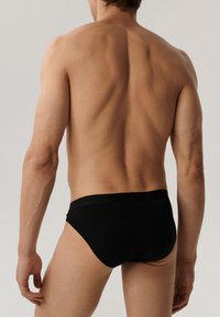 Czarne slipy męskie o gładkiej teksturze, elastycznym pasie i minimalistycznym designie, prezentowane od tyłu na neutralnym tle.