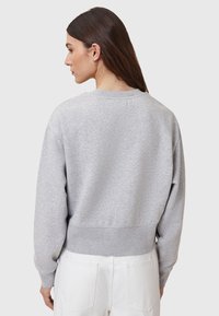 Grijze katoenen sweatshirt met ronde hals, verlaagde schouders en geribbelde onderkant. De achterkant toont een zachte textuur en een relaxte pasvorm. Gecombineerd met witte broeken.