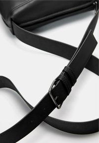 Crna kožna crossbody torba ravnog oblika, s podesivim remenom i detaljem metalne kopče. Ima glatku teksturu i minimalistički dizajn.
