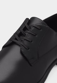 Μαύρο δερμάτινο παπούτσι φορέματος με κλειστό κορδόνι και λεπτή ραφή λεπτομέρειας στο λείο επάνω μέρος και στην άκρη της σόλας.