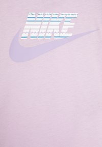 Jasnofioletowa koszulka z dużym logo „Nike” w niebiesko-białym wzorze, obok jednostajnego fioletowego logo swoosh.