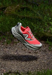 Chaussure de sport orange vif avec une tige texturée et une semelle blanche rembourrée ; présente des accents gris et un logo "N" bien en vue.