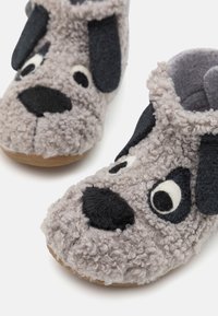 Pantofole grigie e soffici che sembrano il muso di un cane, con dettagli neri per orecchie, occhi e naso. Materiale morbido con design slip-on.