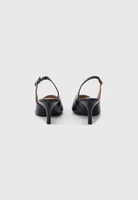 Ζευγάρι μαύρες δερμάτινες γόβες με λουράκι στο πίσω μέρος και ρυθμιζόμενα λουράκια στον αστράγαλο, προβολή από πίσω σε λευκό φόντο.